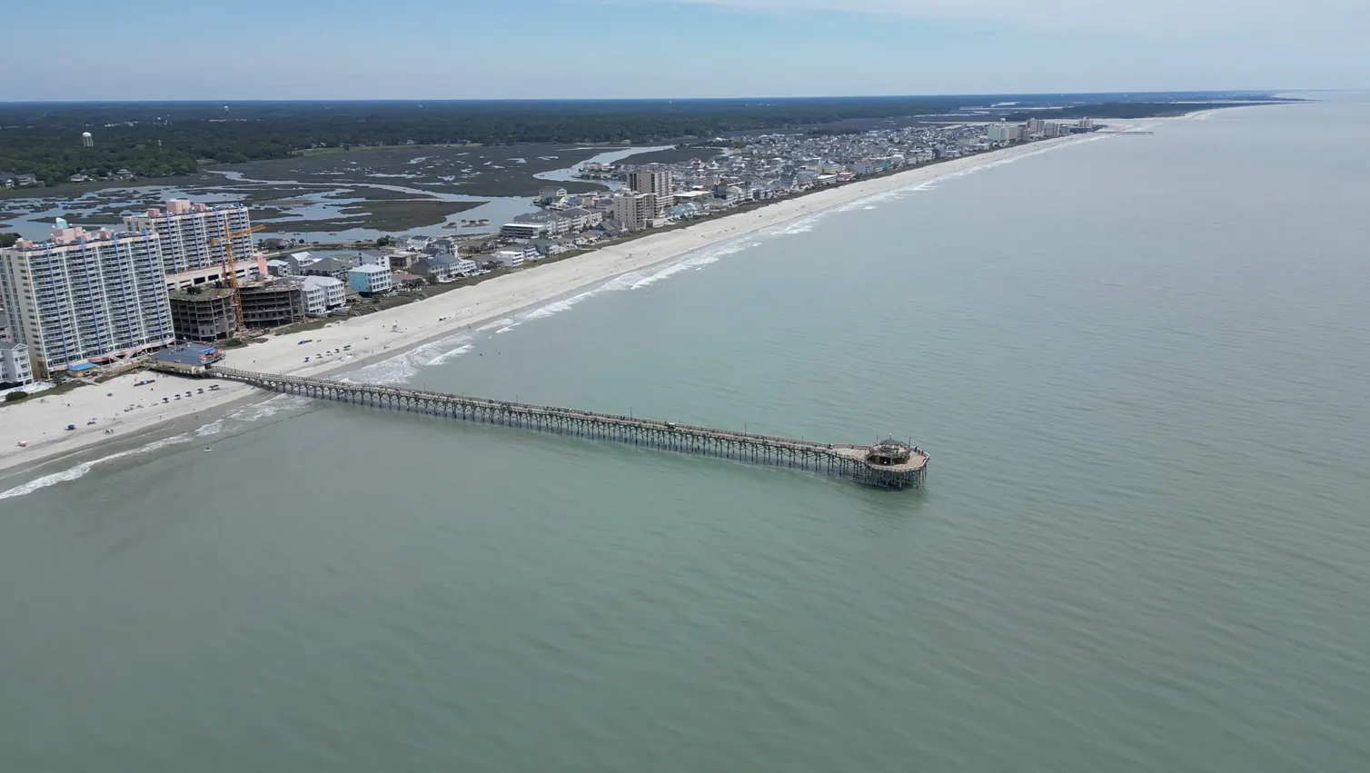 Aerial view of the North Myrtle Beach oceanfront, with a fishing pier, beachfront towers and the salt marsh behind them